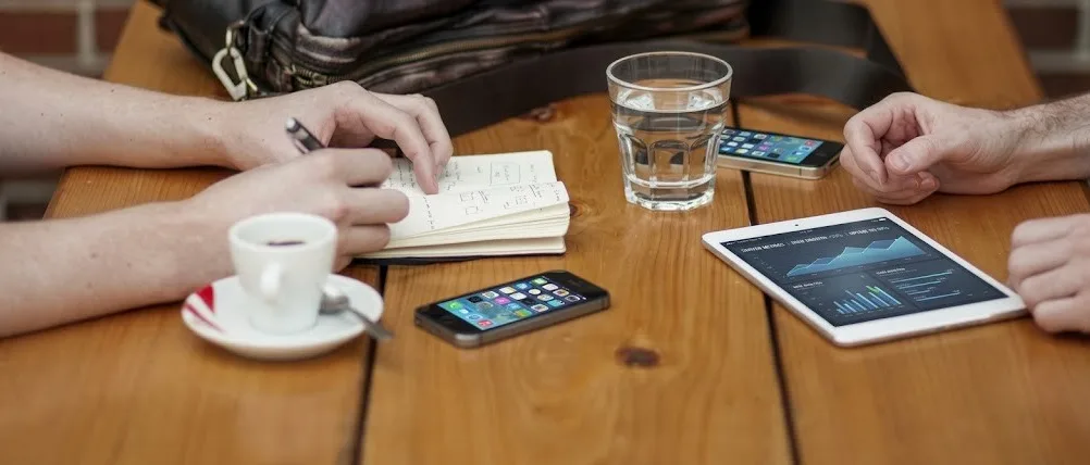 Schůzka u stolu s tabletem, telefony a zápisníkem